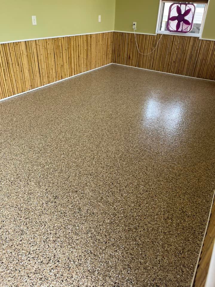 Room with speckled flooring, wood panel walls, and a fan in the window.