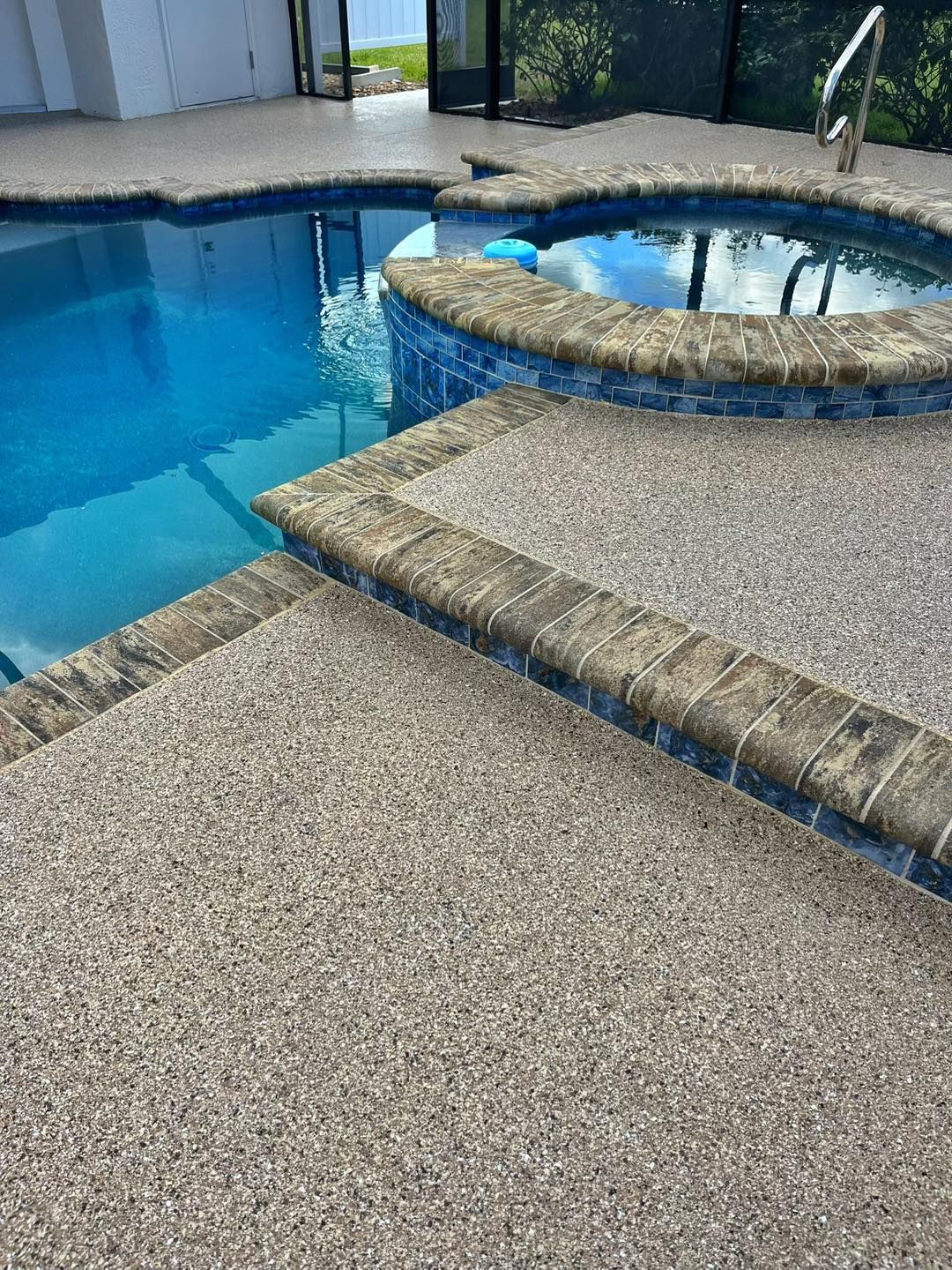 Pool and spa with pebbled deck, blue water, and brick coping.