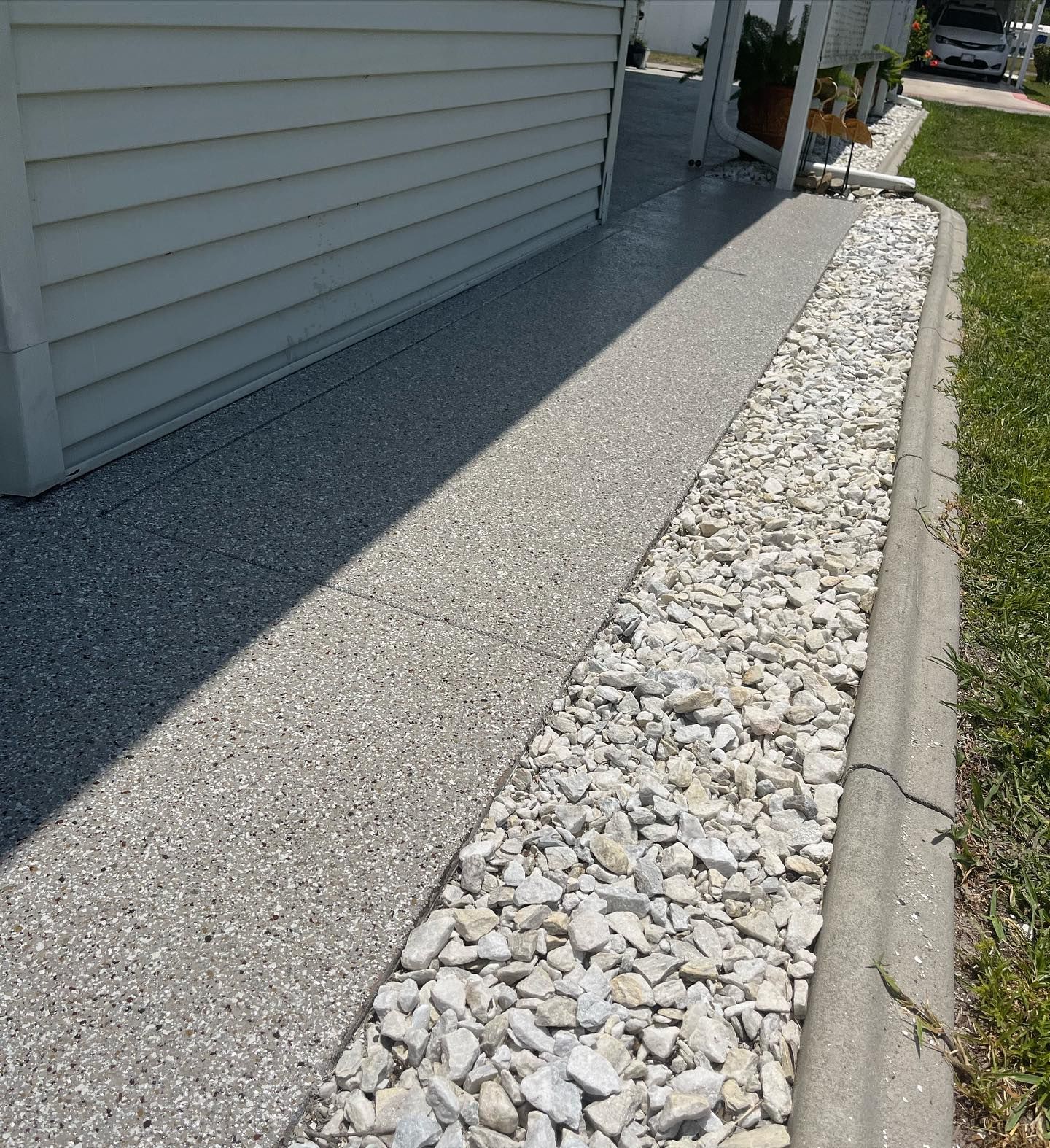 Concrete walkway with a gravel bed border next to a white house.