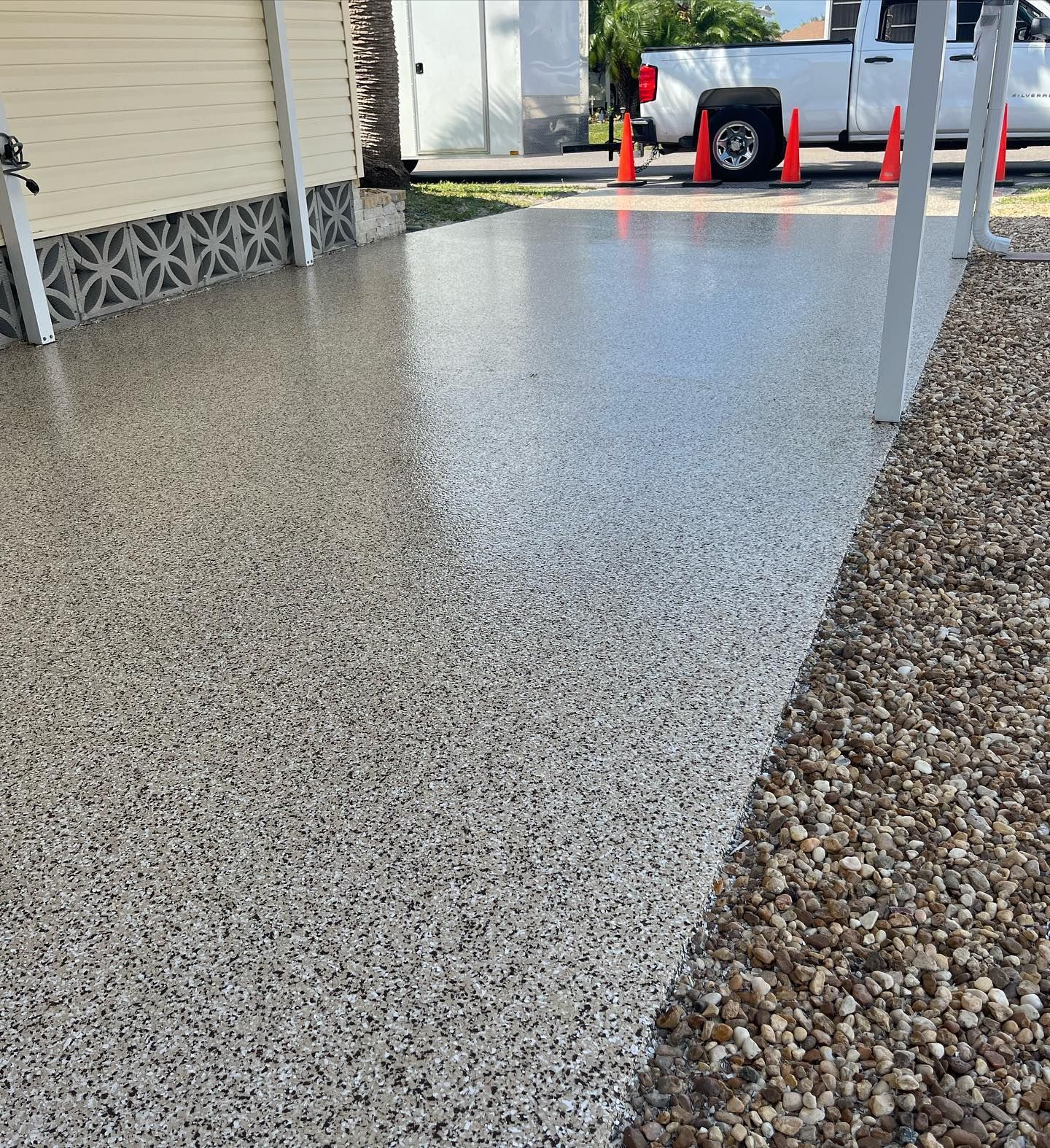 Polished, speckled concrete driveway with gravel border next to a house.