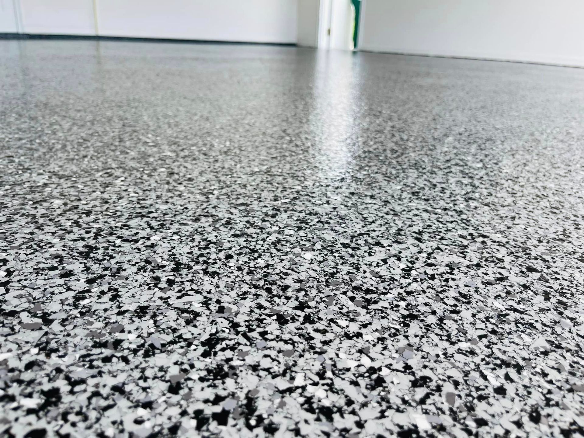 Close-up of a speckled, gray epoxy floor. Shiny, with light reflecting off the surface.