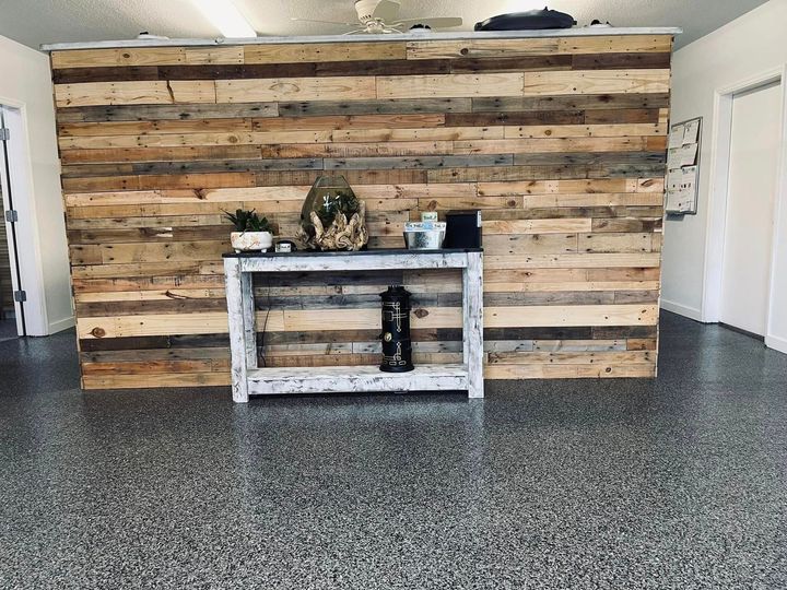 Reception area with a reclaimed wood wall, white table, and speckled gray floor.