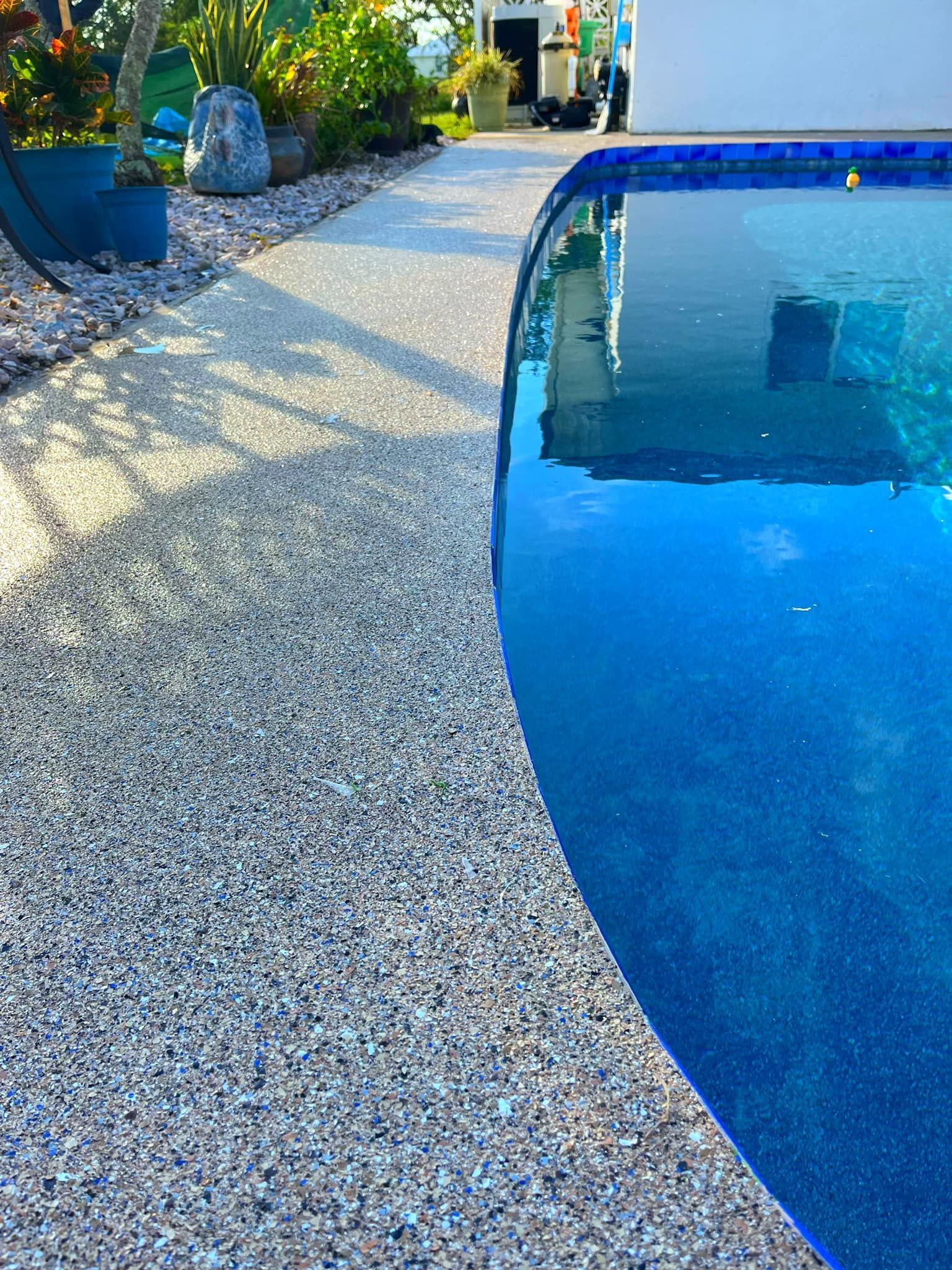 Poolside view of a curved pool with blue water next to a textured, gray concrete walkway.