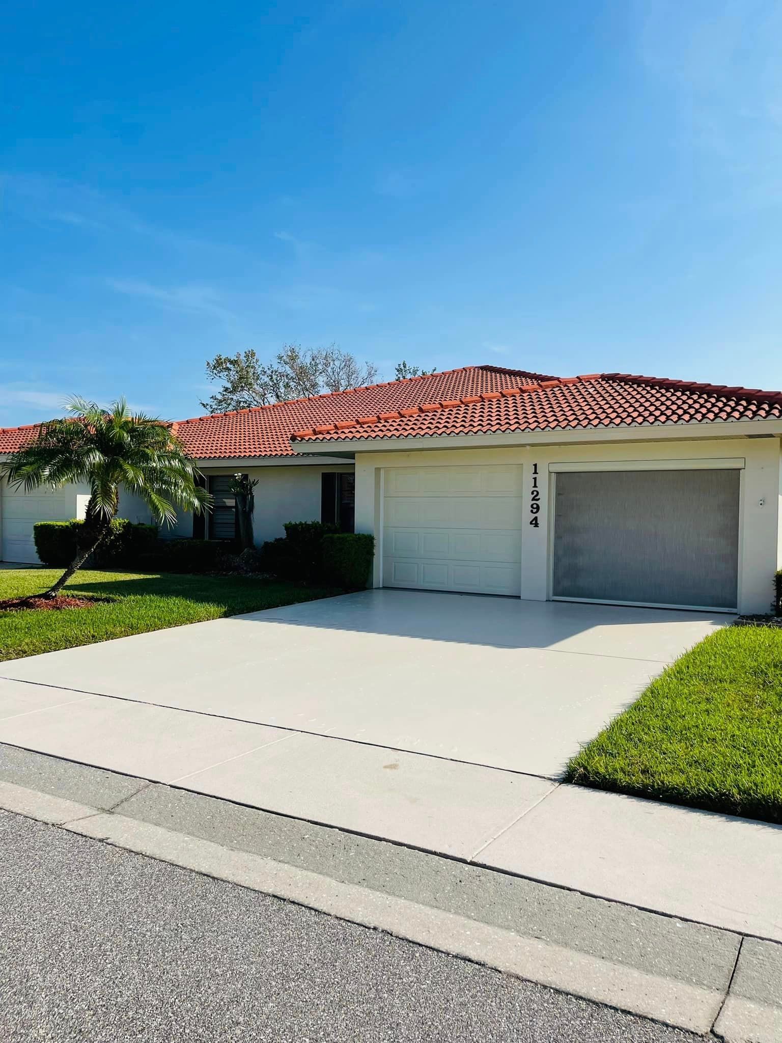Single-story home with red tile roof, white garage door, and a paved driveway under a blue sky.