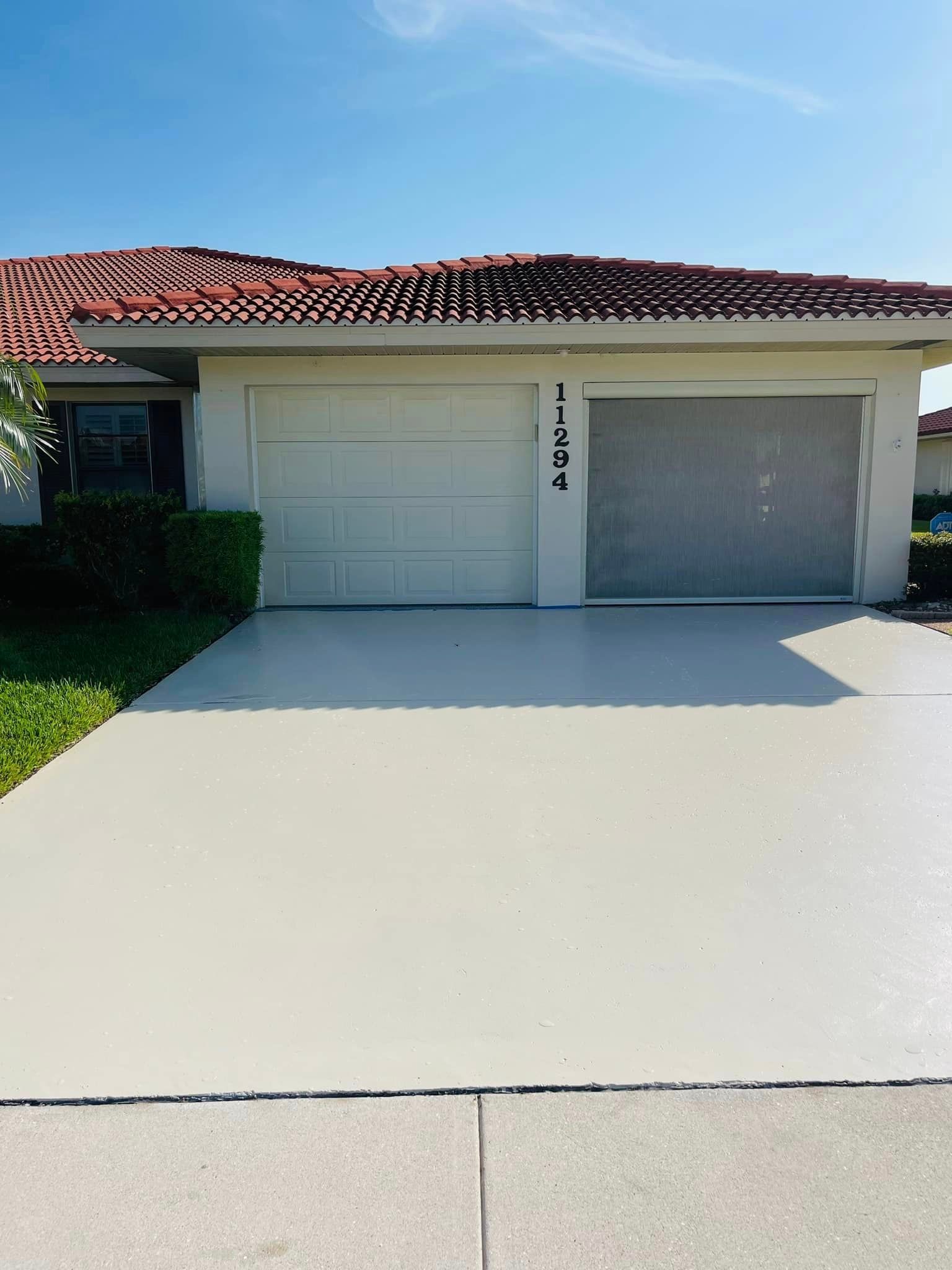 House with light gray driveway and garage doors, red tile roof, and green shrubbery. Address number is 11574.