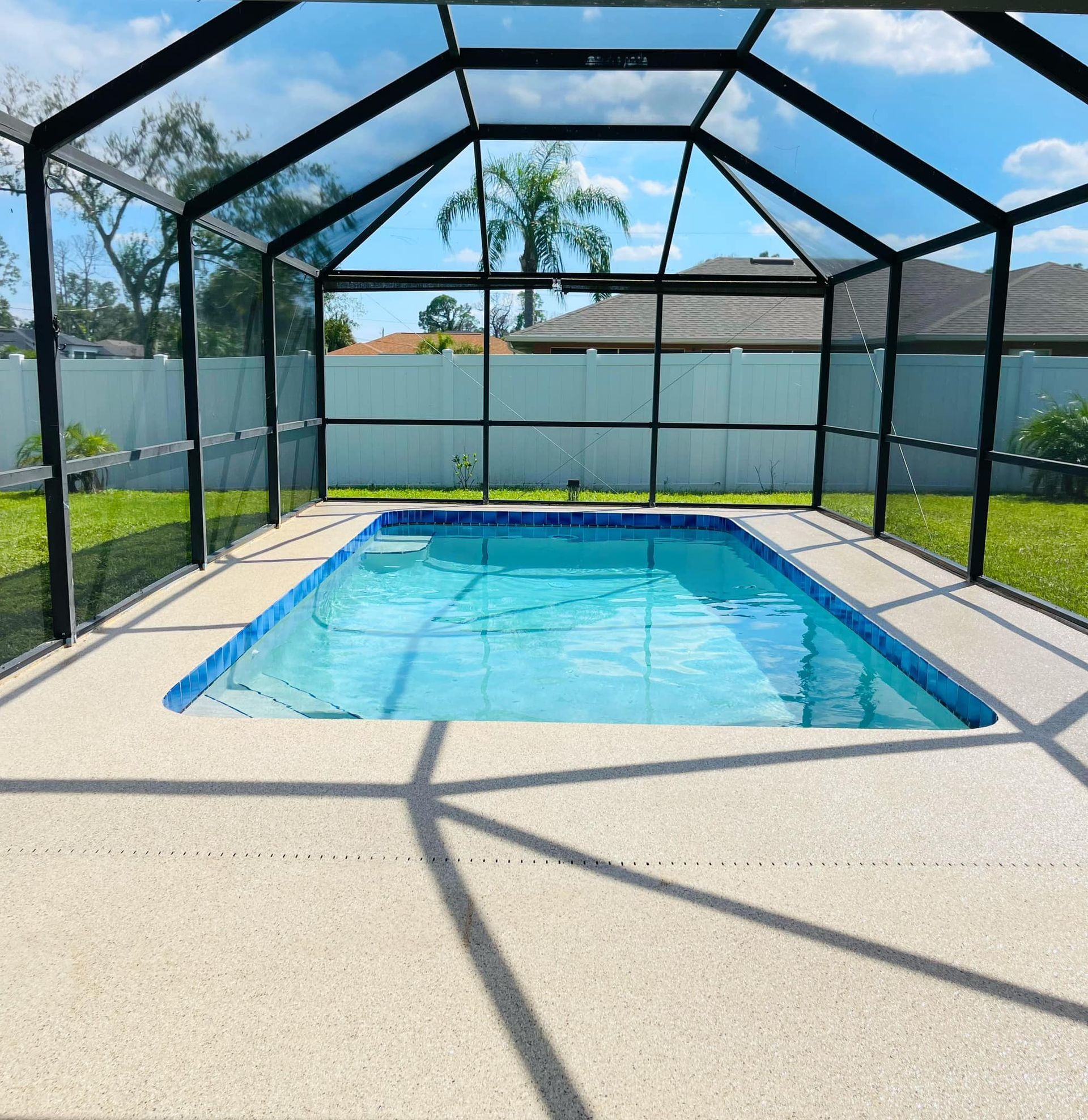 Pool enclosed in black mesh with blue water, surrounded by a light-colored patio, green grass, and a white fence.