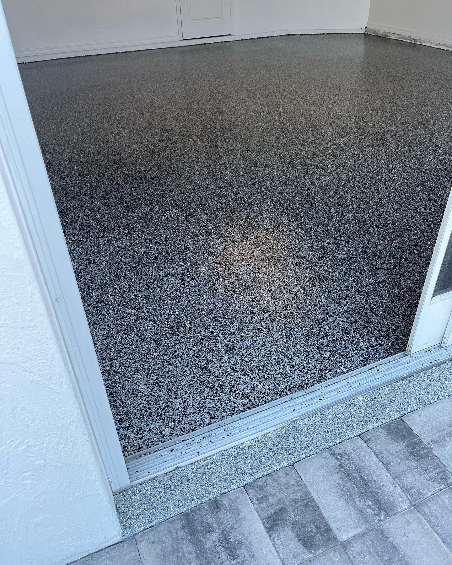Garage with speckled gray epoxy flooring, viewed from a doorway onto a patio.