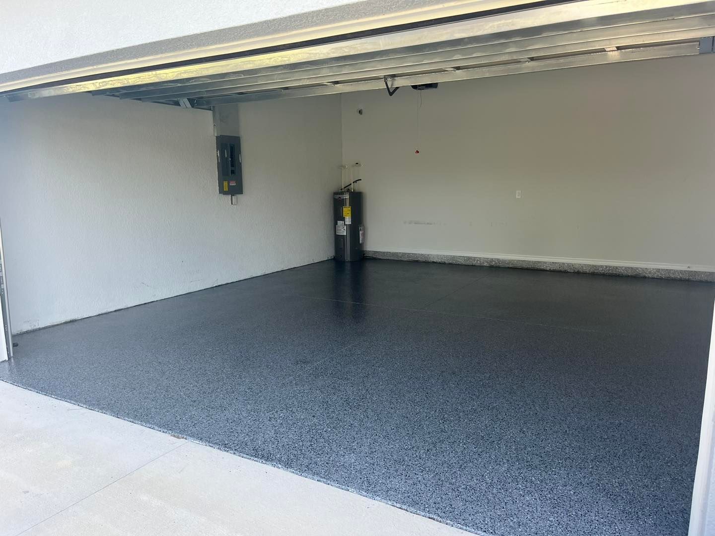 Empty garage with epoxy floor, water heater, and electrical panel.