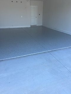 Empty garage with a gray epoxy floor. A white door is visible in the distance.