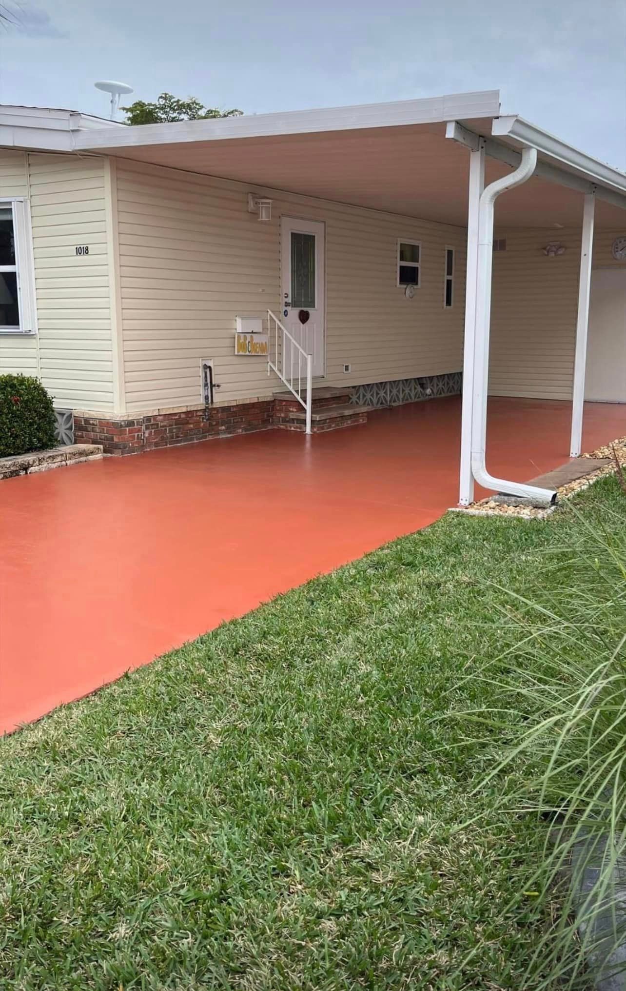Beige house with orange-painted walkway and carport, white gutters, and green grass.