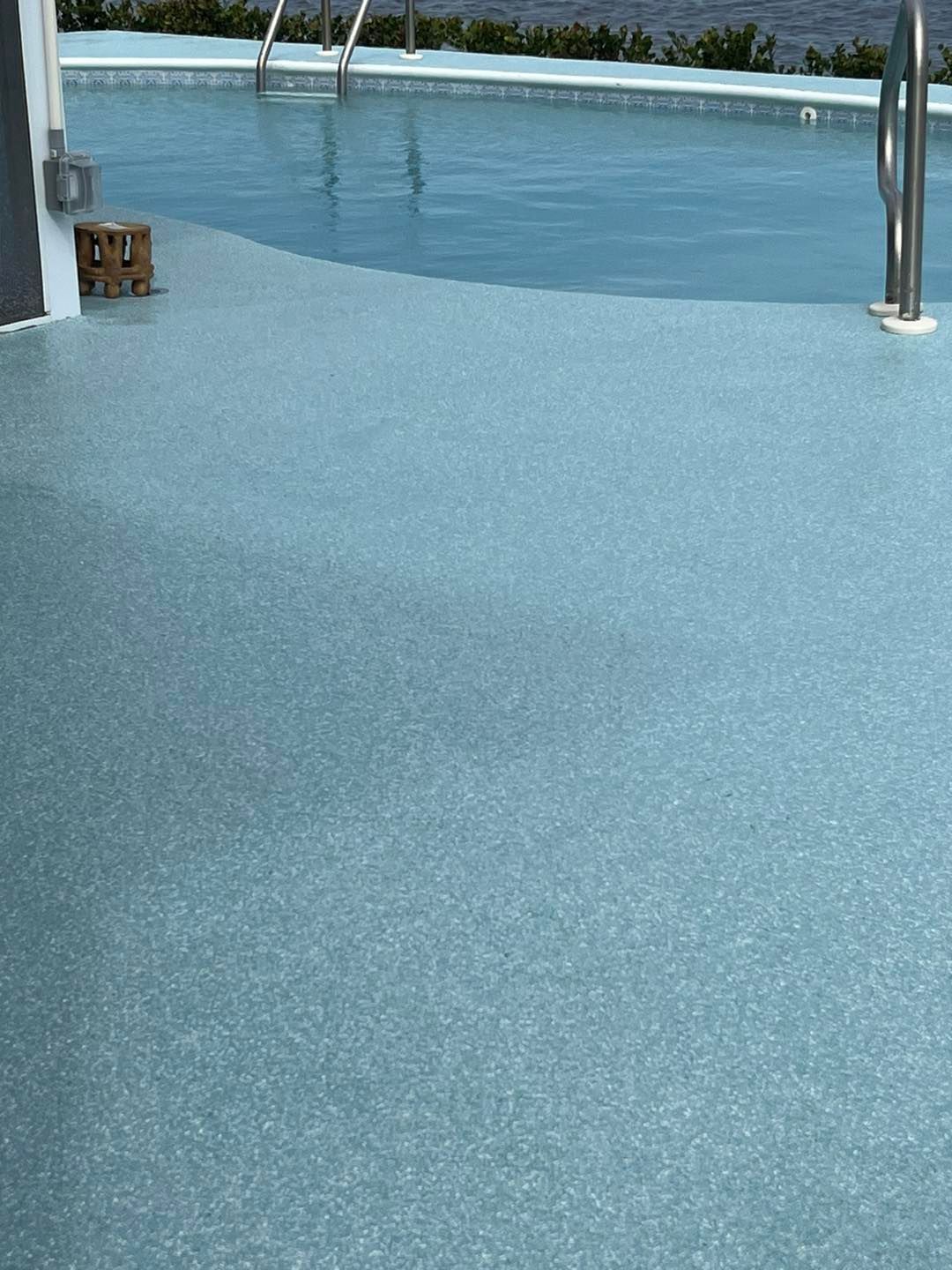 Blue speckled pool deck next to a pool with chrome railings.