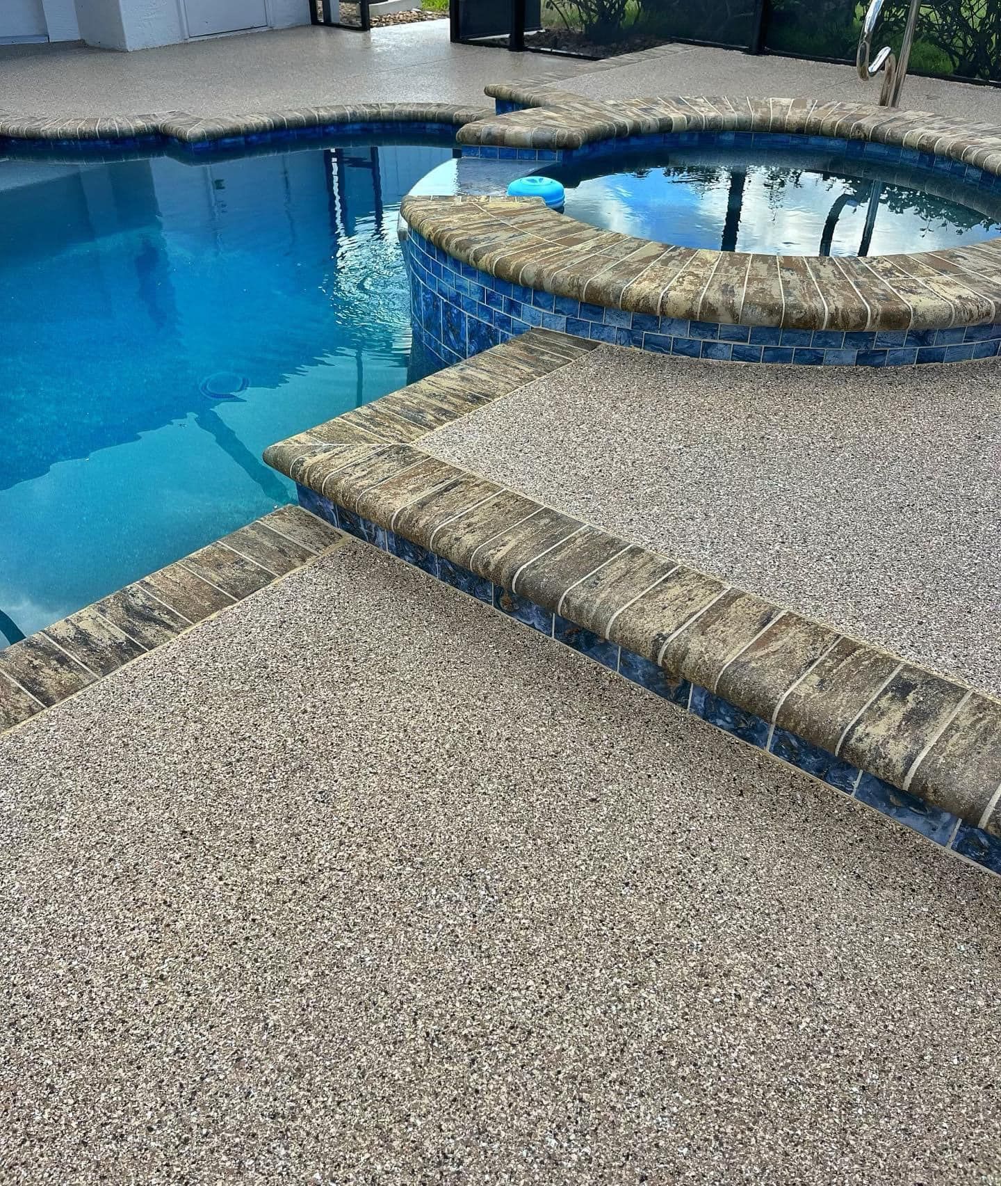 Pool deck with speckled concrete, a blue pool, and a raised hot tub.
