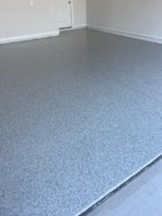Gray epoxy-coated garage floor, speckled with darker chips. The floor reflects ambient light.