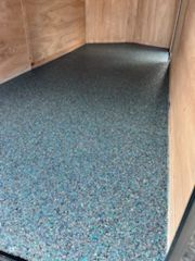 Inside of a horse trailer, a textured blue-green flooring covers the base between wooden walls.