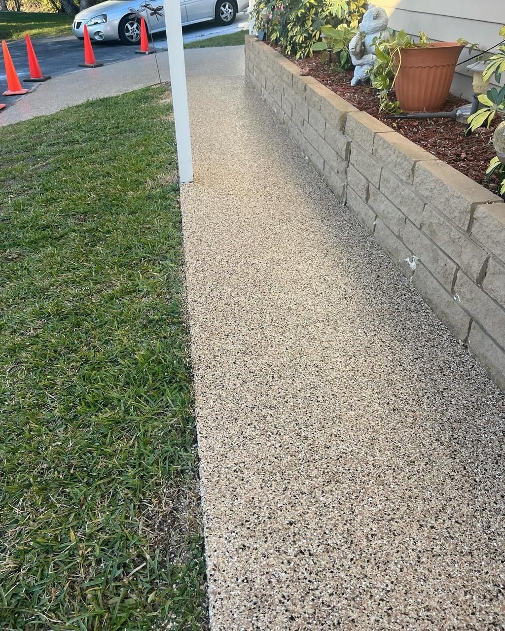 Gravel walkway beside a lawn and a retaining wall with plants; a car and cones are in the background.