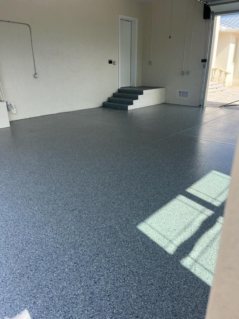 An empty garage with a blue speckled floor. Steps lead to a doorway, sunlight shines in.