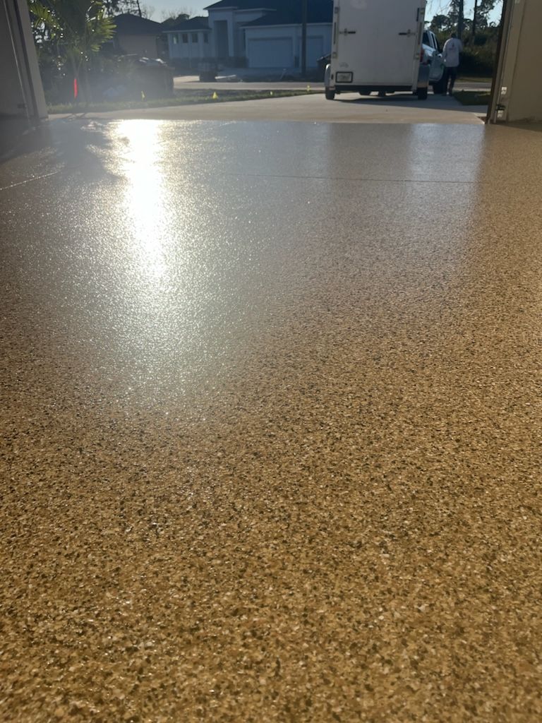 Shiny tan-colored concrete floor reflecting sunlight, with a white truck and residential area in the background.
