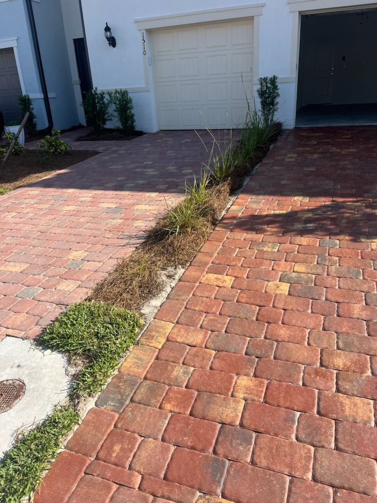 Brick driveways with a strip of dead plants in between, leading to a garage.