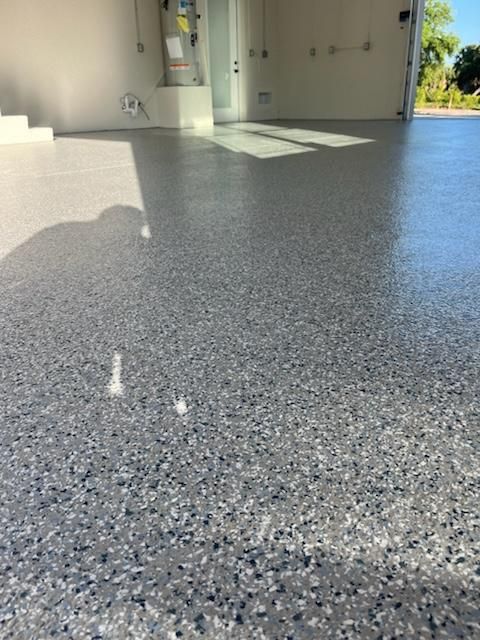 Epoxy-coated garage floor with gray and speckled aggregate finish. Sunlight floods the empty space.