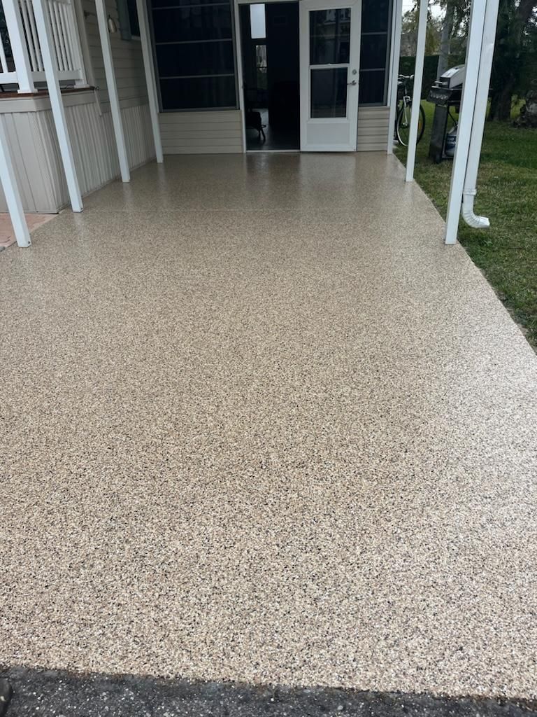 A covered porch with a speckled floor, leading to a door.