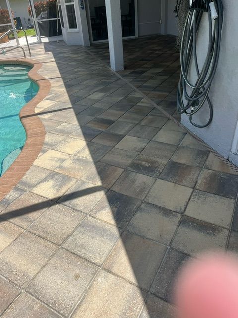 Patio with tiled pathway next to a pool. Hose attached to a wall.