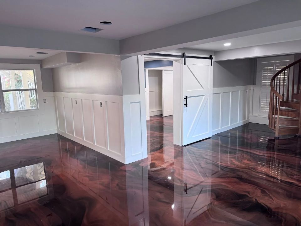 Room with red and gold epoxy floor, white paneled walls, and a barn door, with a spiral staircase visible.