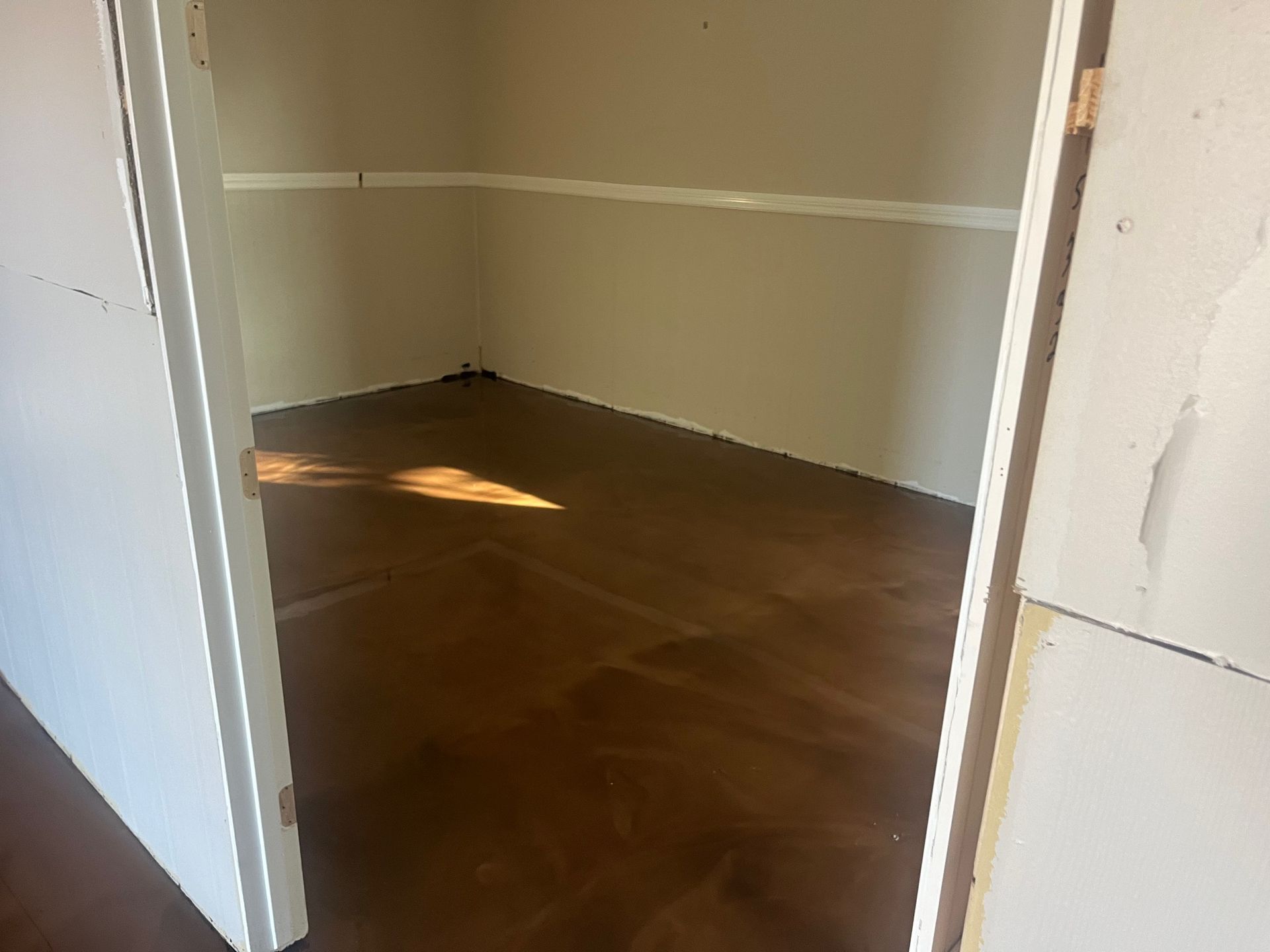 Empty closet with wood floor and white walls. Doorway in the foreground. Sunlight on floor.