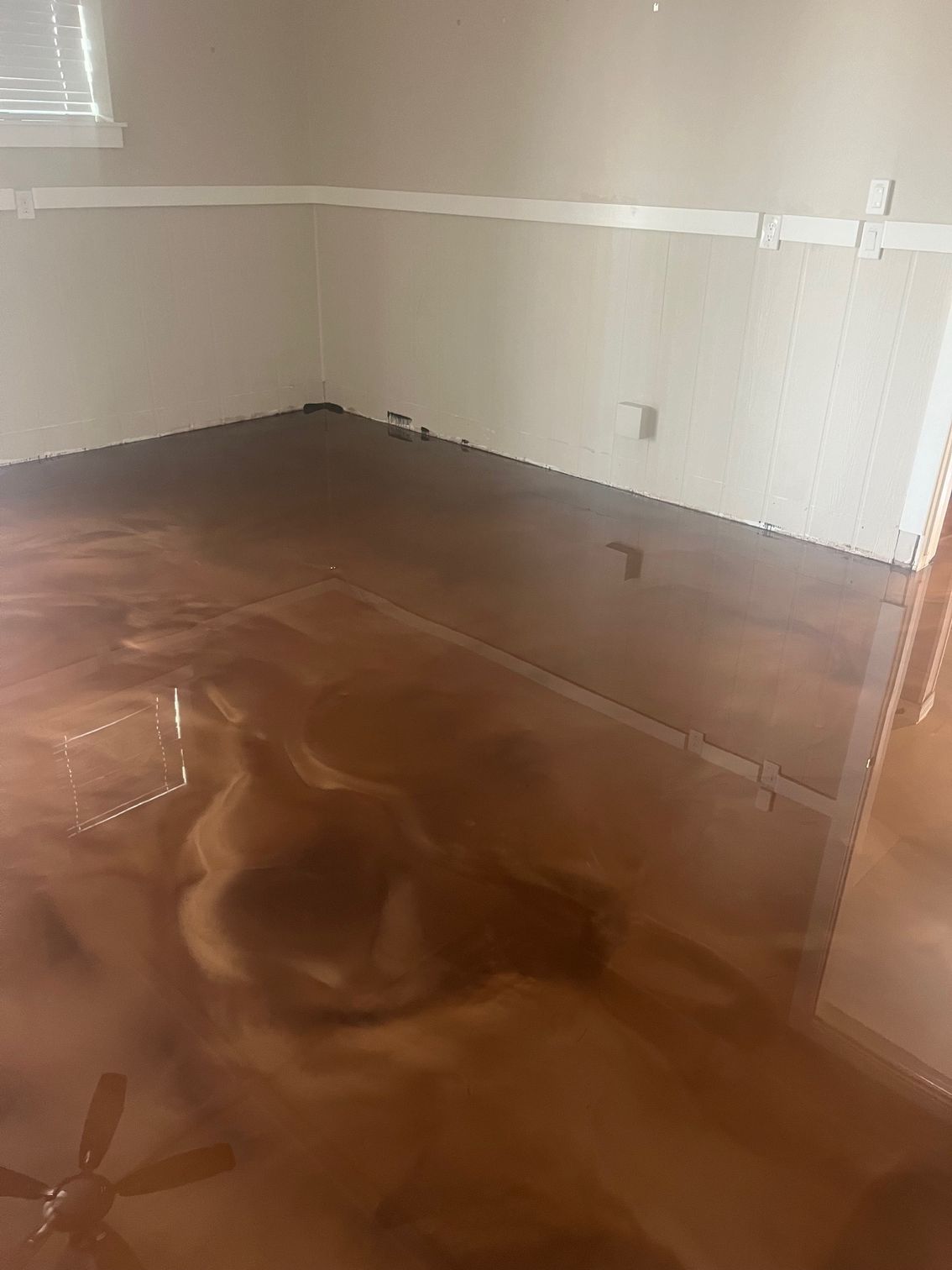 Brown metallic epoxy floor in a room, reflecting light with swirling patterns. White walls and trim.