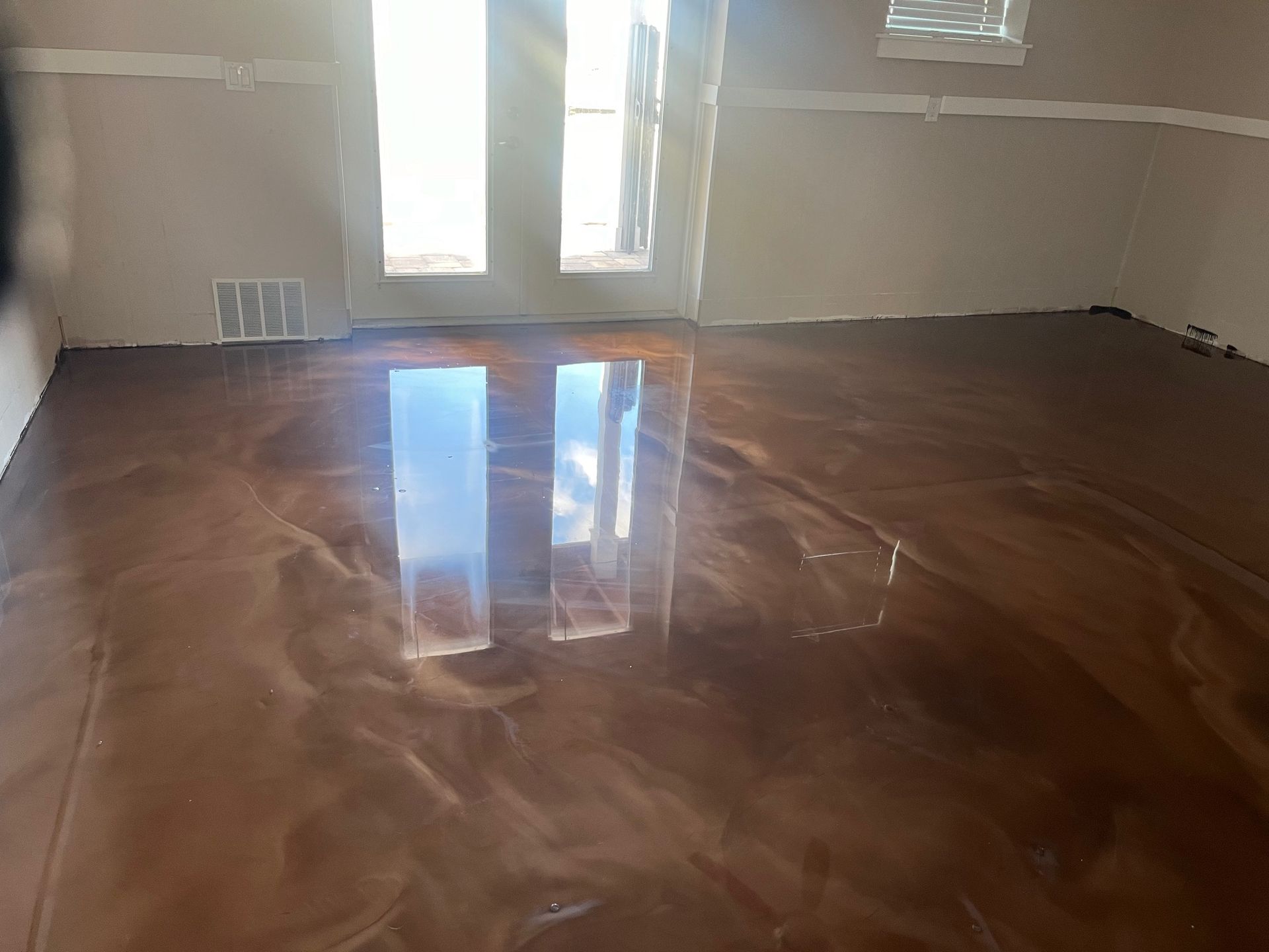Brown metallic epoxy floor with reflections, in a room with a window and door.