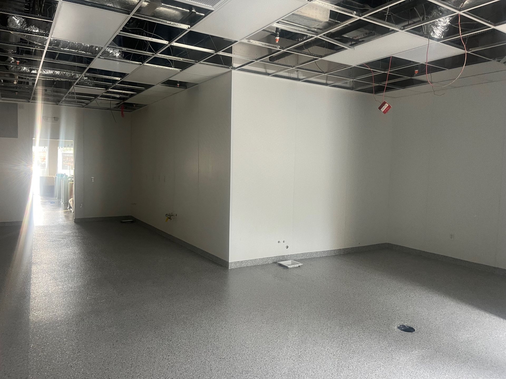 Empty room with a grid ceiling, gray floor, and white walls.