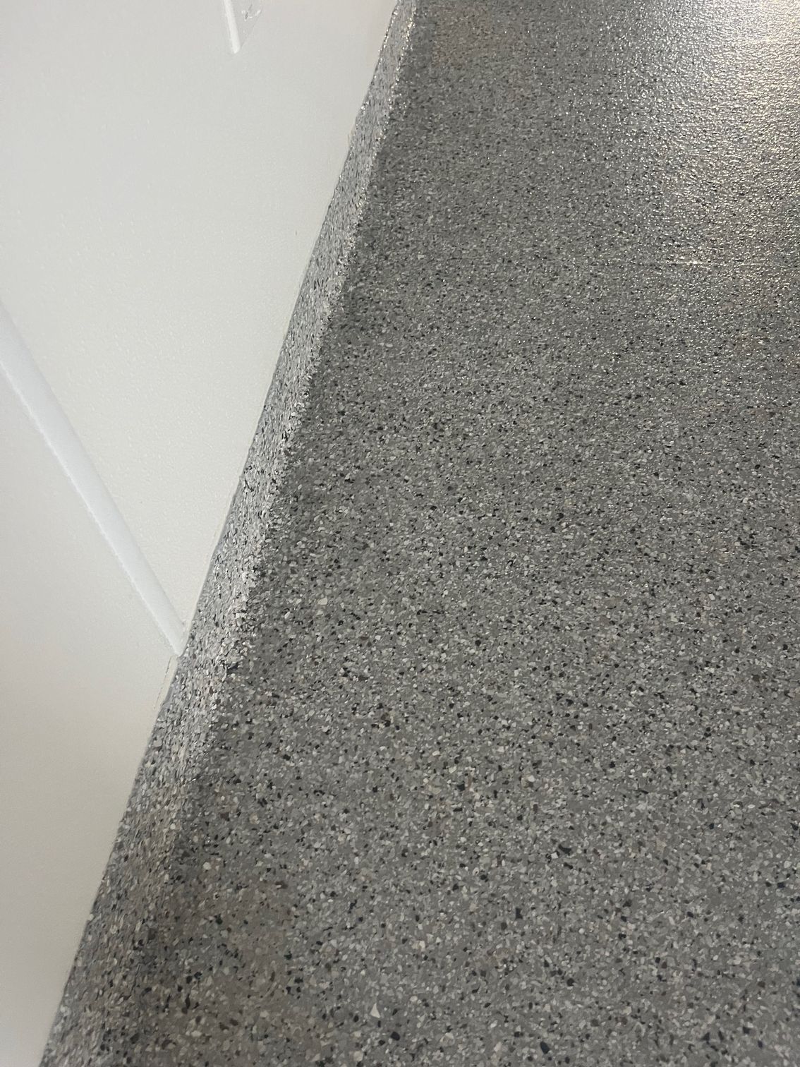 Gray speckled concrete floor next to white wall.