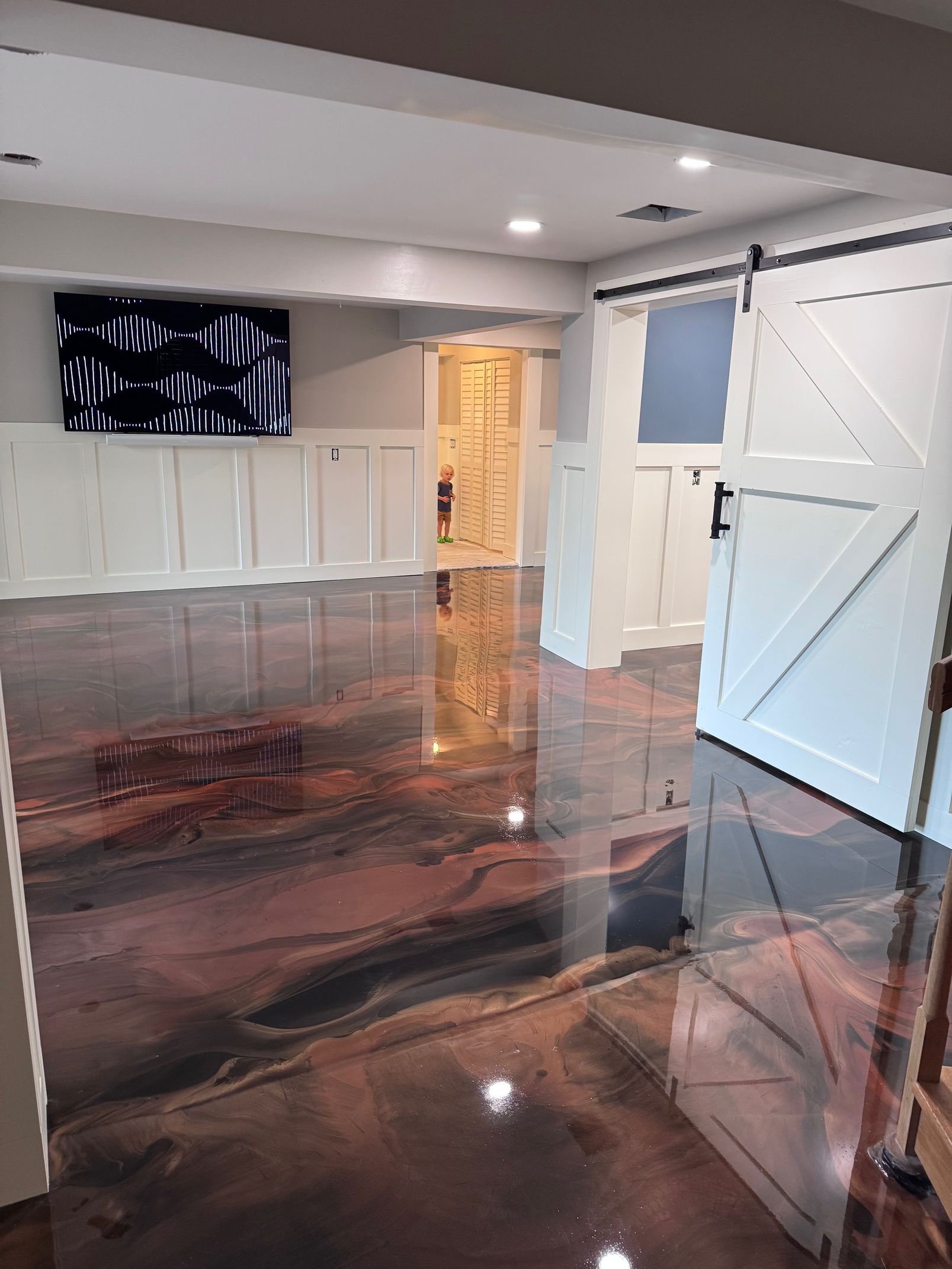 Room with metallic-colored epoxy floor, white paneled walls, a TV, and open barn doors.