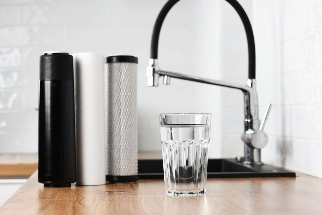 Bancone da cucina moderno con caraffe filtranti e un bicchiere sotto il rubinetto cromato.