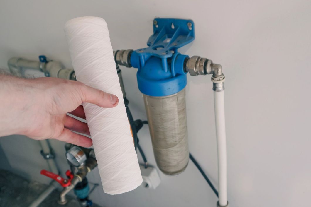 Una mano che regge una cartuccia filtrante bianca accanto a un sistema di filtraggio dell'acqua blu con tubi.