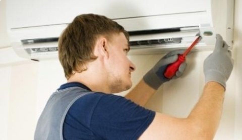Un tecnico utilizza un cacciavite rosso per riparare un condizionatore d'aria a parete all'interno di un edificio.