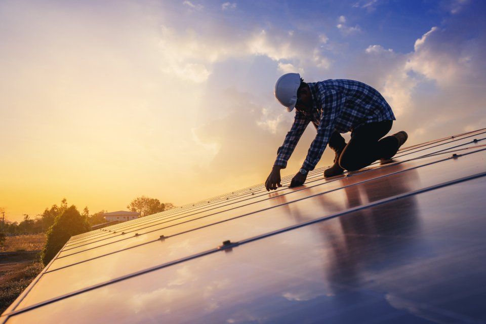 Operaio inginocchiato su un tetto mentre installa pannelli solari al tramonto