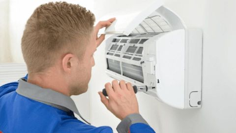 Tecnico pulisce il filtro di un condizionatore d'aria bianco a parete.