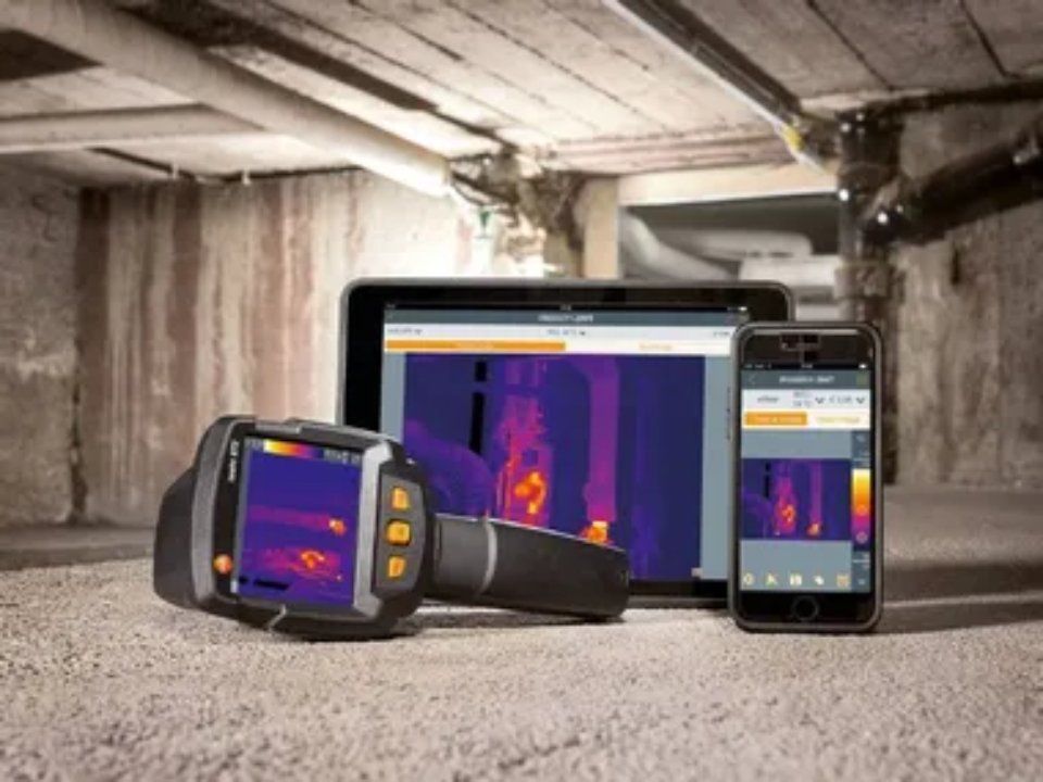 Termocamera, tablet e smartphone che visualizzano mappe termiche in una stanza di cemento.