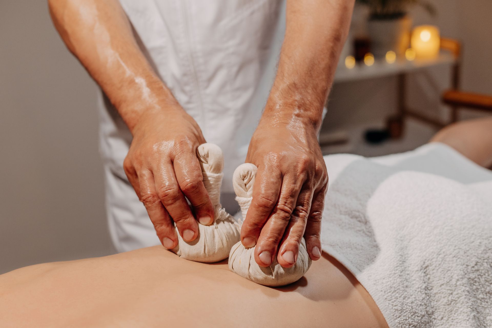 Therapist massaging a person's back with herbal compress balls in a spa setting - Thames, NZ - Thai Classic Massage Thames