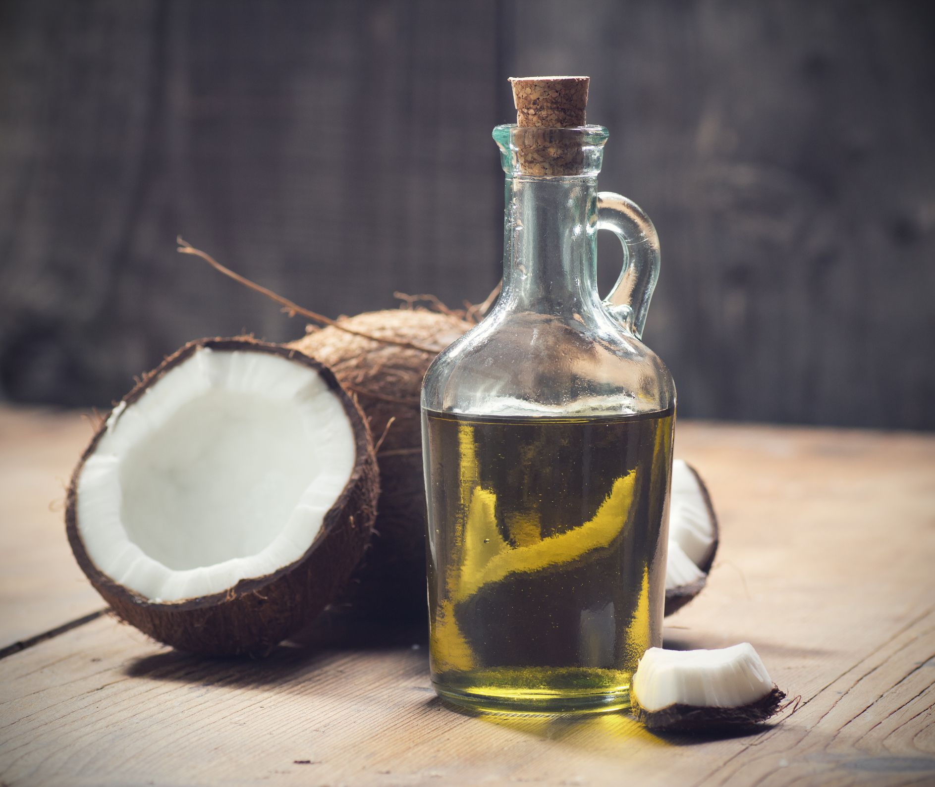 Coconut oil in a glass bottle with a cork, next to halved coconuts on a wooden surface - Thames, NZ - Thai Classic Massage Thames