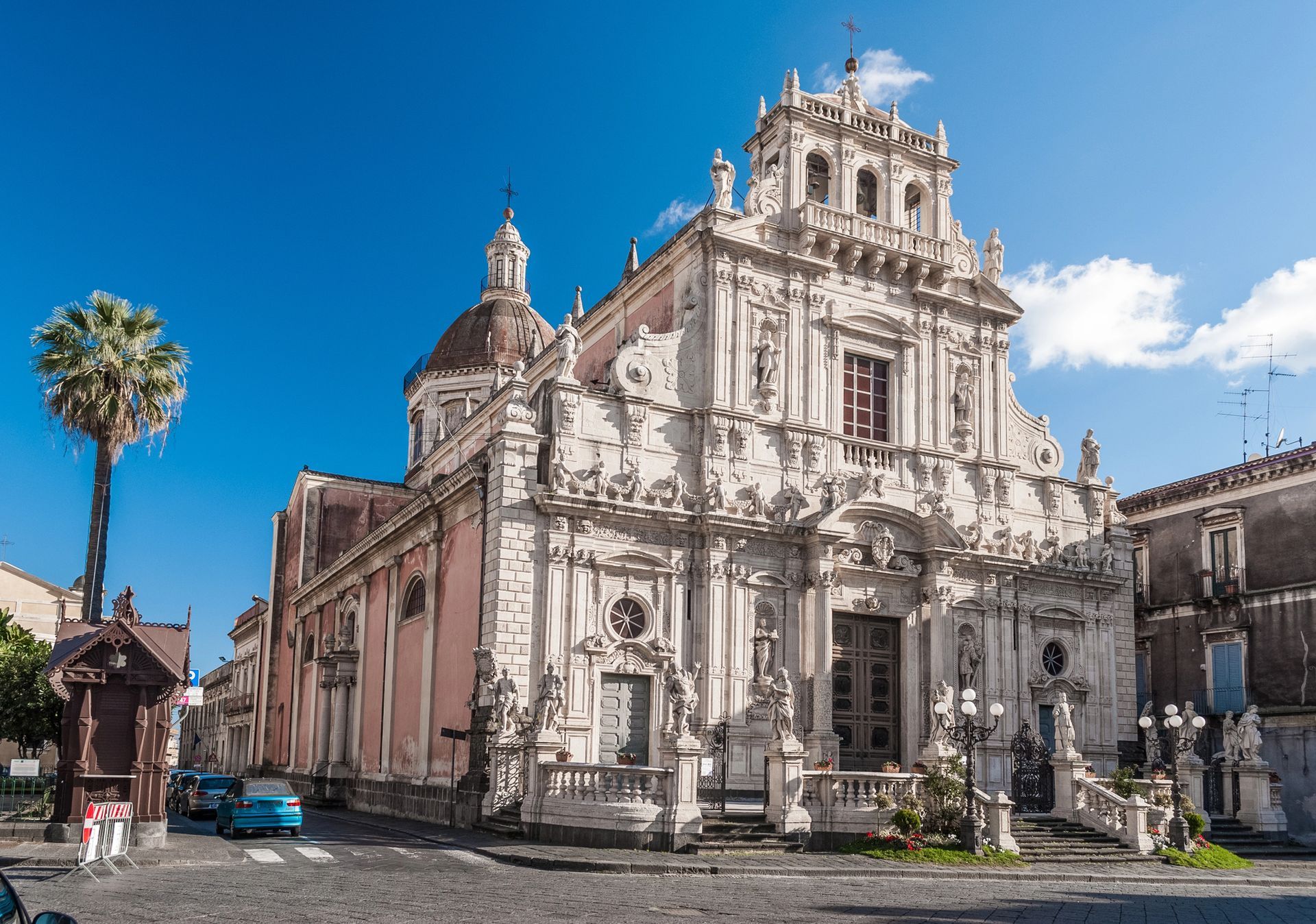 Facciata di una chiesa storica riccamente decorata, con una palma sullo sfondo di un cielo azzurro brillante.