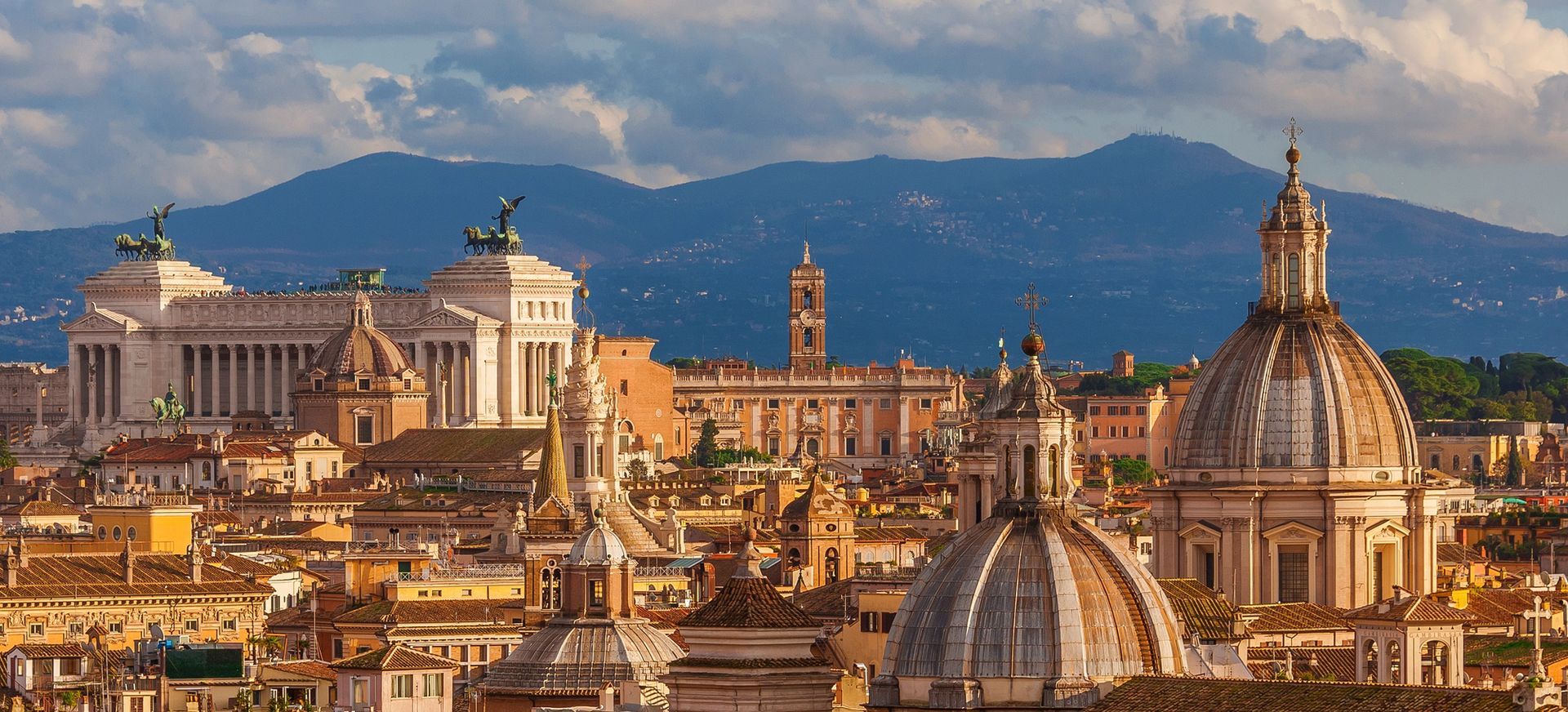 Veduta panoramica delle cupole e dei tetti di Roma al tramonto, con la Basilica di San Pietro sullo sfondo.