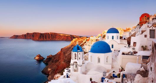 Edifici bianchi con cupole blu su una scogliera a picco sul mare al tramonto, Santorini, Grecia