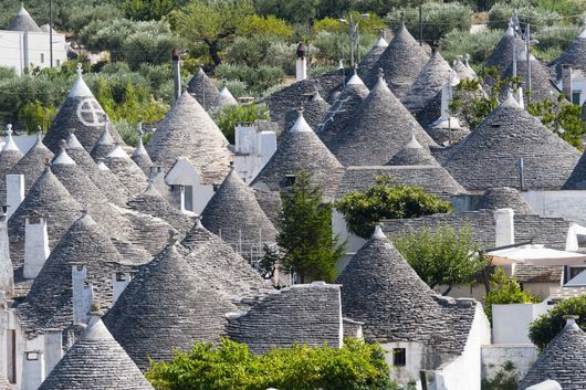 Gruppo di tetti conici in pietra grigia tra alberi verdi in un villaggio collinare