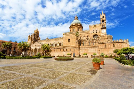 Cattedrale storica in pietra con cupola e campanile sotto un cielo azzurro brillante, vista da una piazza lastricata