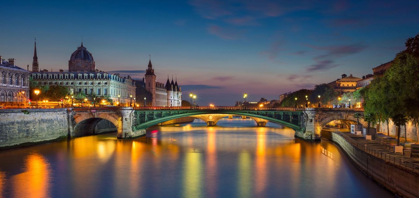 Il fiume cittadino al crepuscolo, con i ponti illuminati e gli edifici storici che si riflettono sull'acqua.