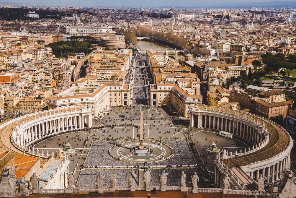 Veduta aerea di Piazza San Pietro e della Basilica nella Città del Vaticano, con Roma che si estende all'orizzonte.