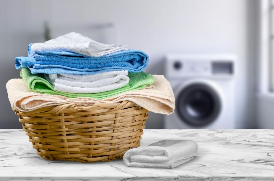 Laundry basket with folded towels and clothes on a table, with a washing machine blurred in the background