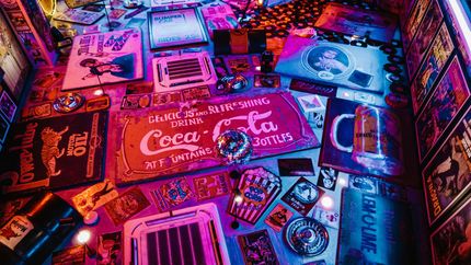 A high-angle shot of various colorful, retro Coca-Cola and vintage advertising signs spread out on a blue-lit surface.