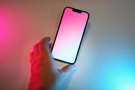 A person's hand reaches for a smartphone displaying a blank white screen, illuminated by red and blue ambient lighting.